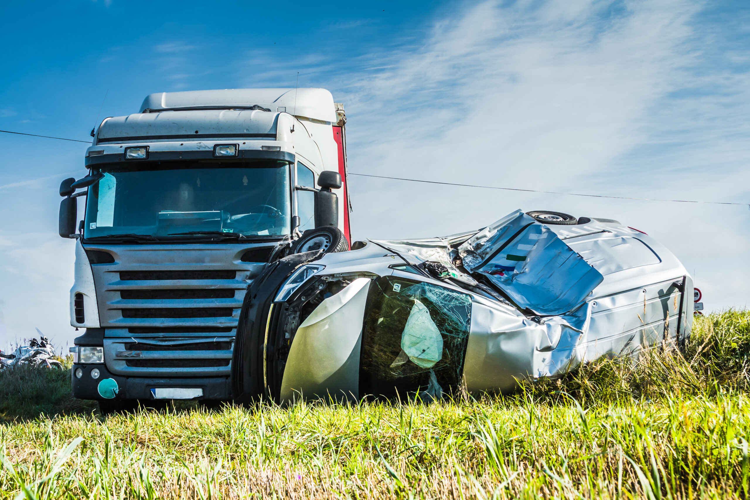 A truck has collided with a car. The car is flipped on its side and has sustained damages to the side of the vehicle and to the hood and windshield. 