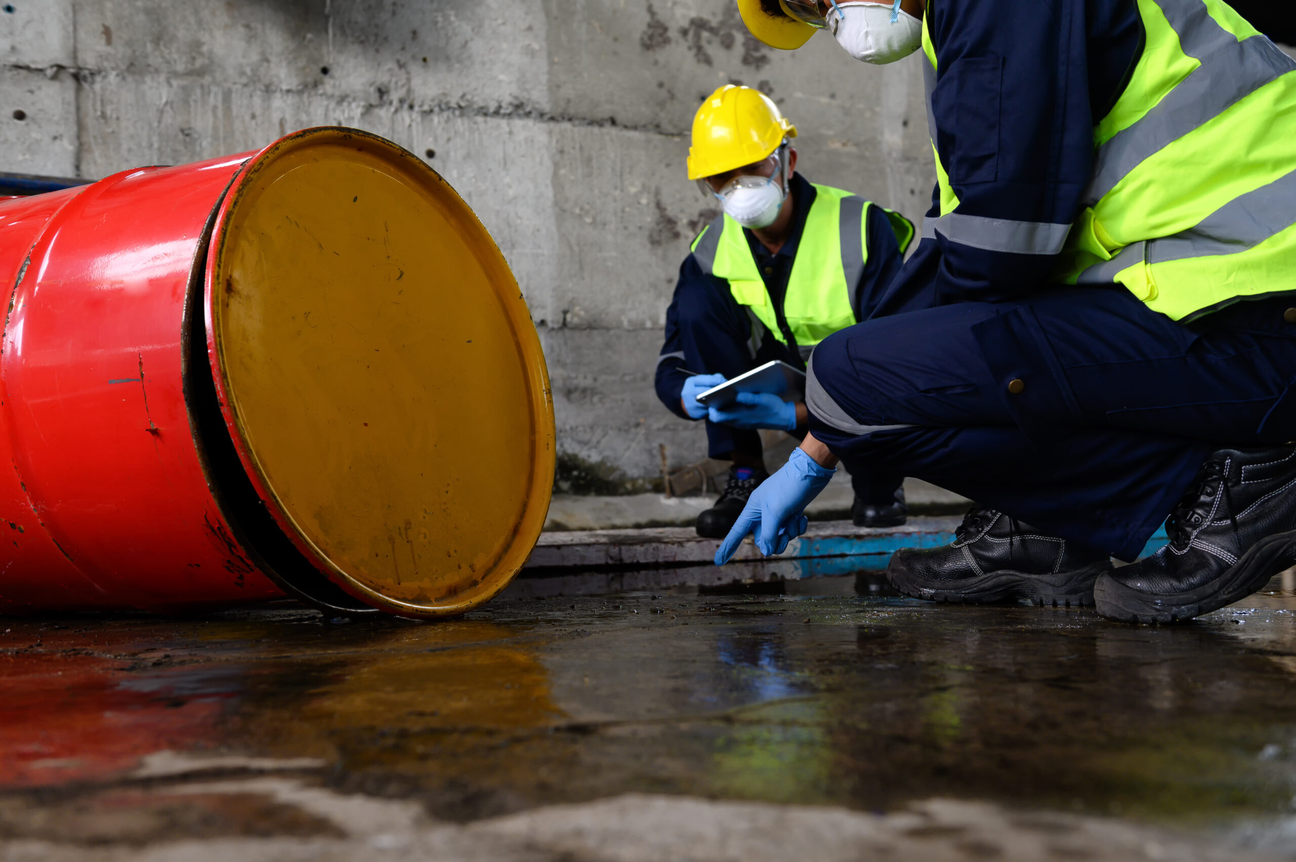 Two industrial workers inspect a chemical spill on the floor of an industrial plant