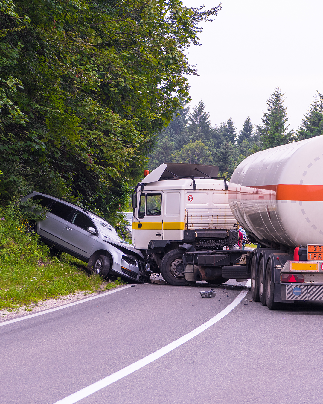 A large truck has collided with an suv on the highway. It was a head on collision and the suv has been shoved by the front of the truck into the trees on the side of the road.