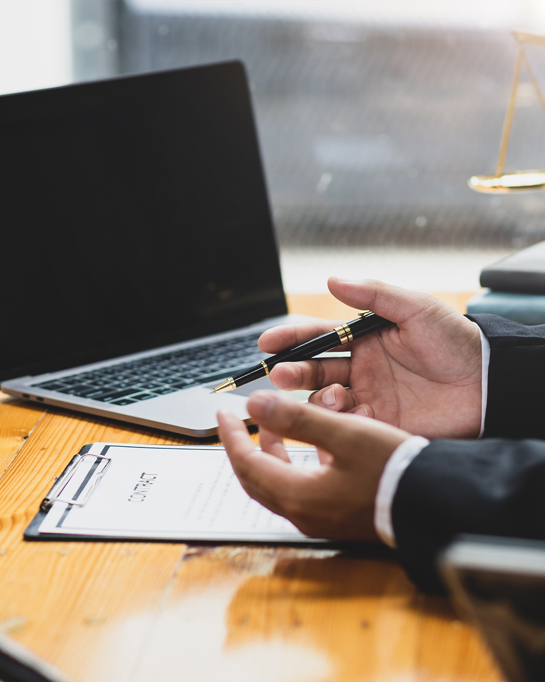 A lawyer holding a pen and sitting in front of a contract at his laptop.