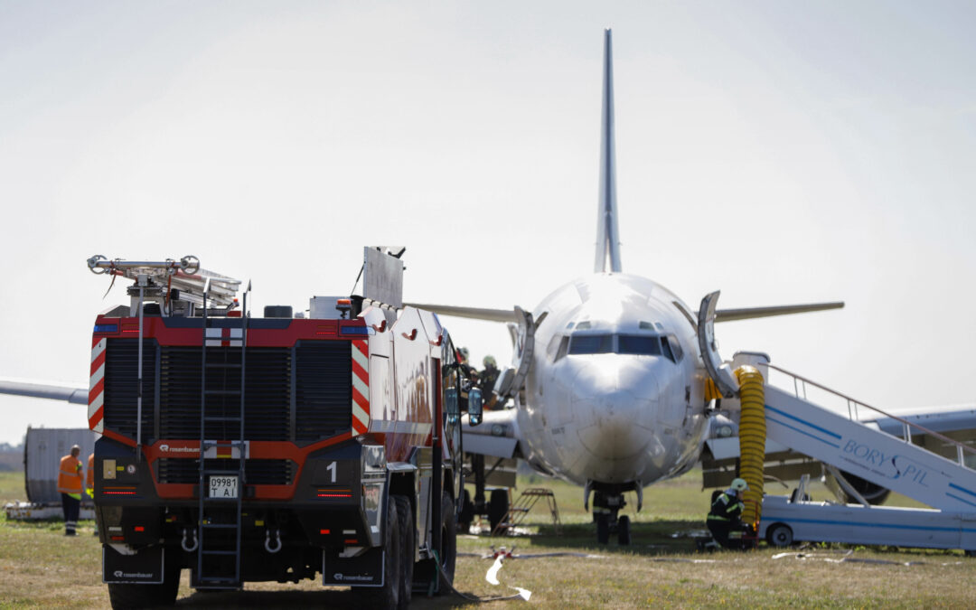 An airplane is grounded on the tarmac. Emergency services are responding and are next to the plane.