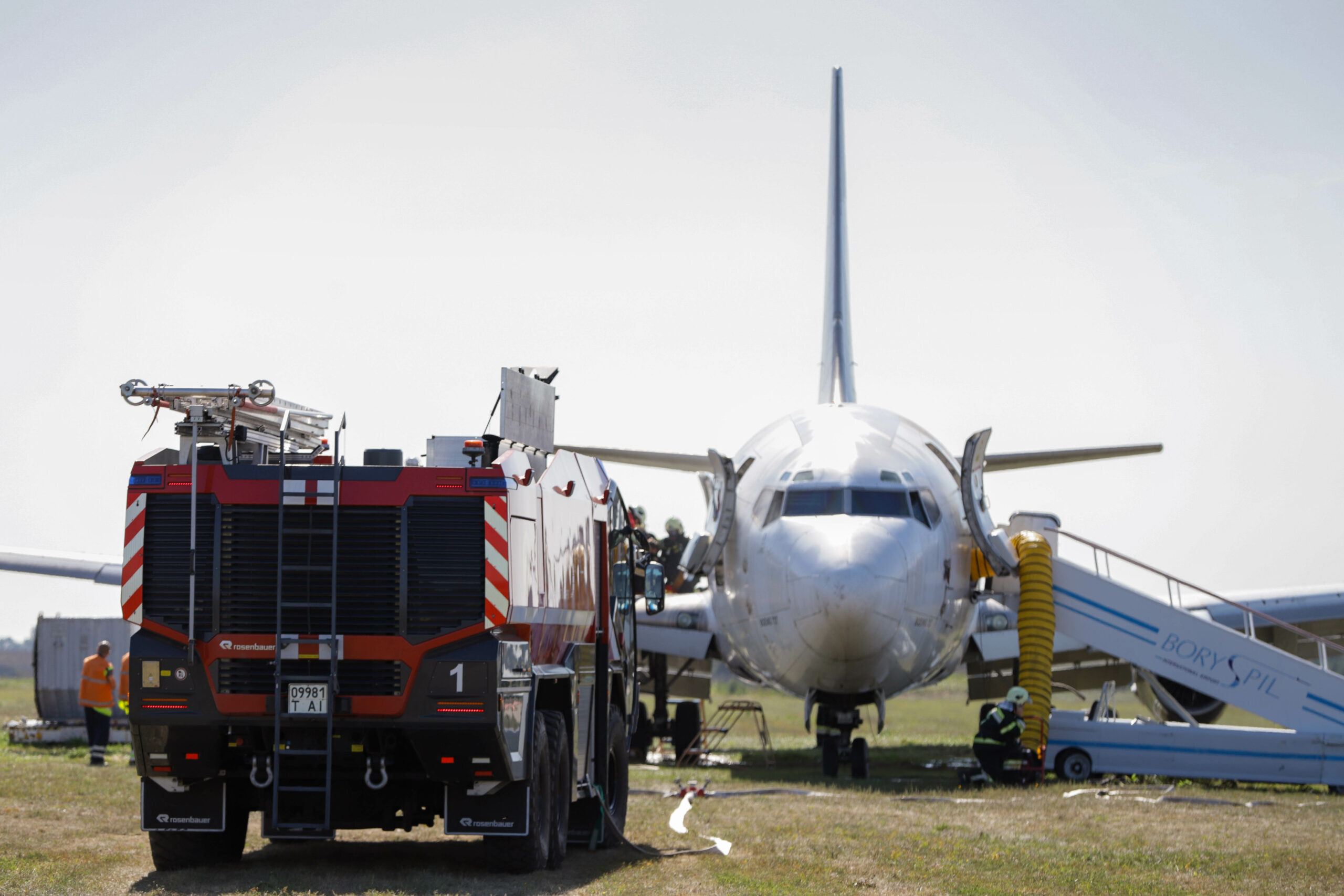 An airplane is grounded on the tarmac. Emergency services are responding and are next to the plane.