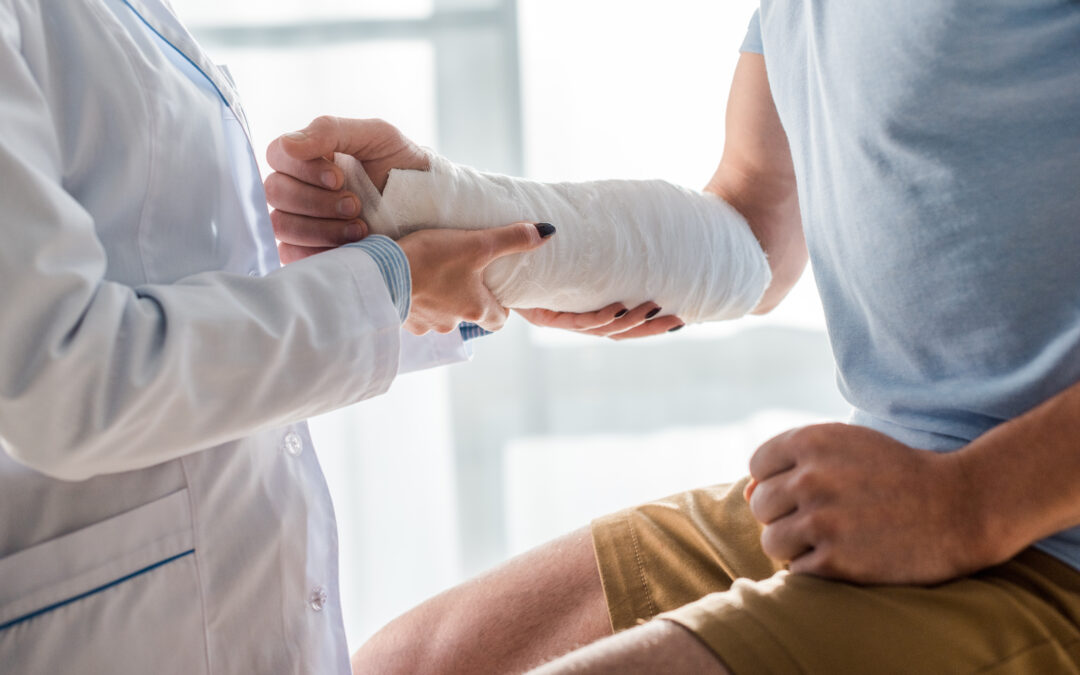 cropped view of orthopedist touching injured arm of man