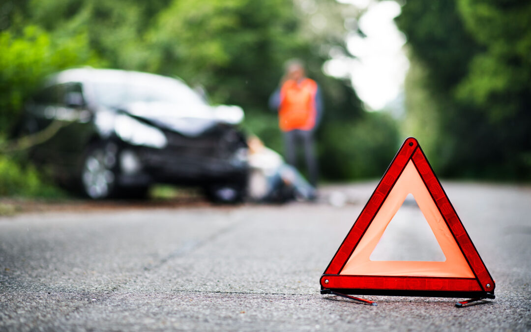 A close up of a red emergency triangle on the road in front of a car after an accident.