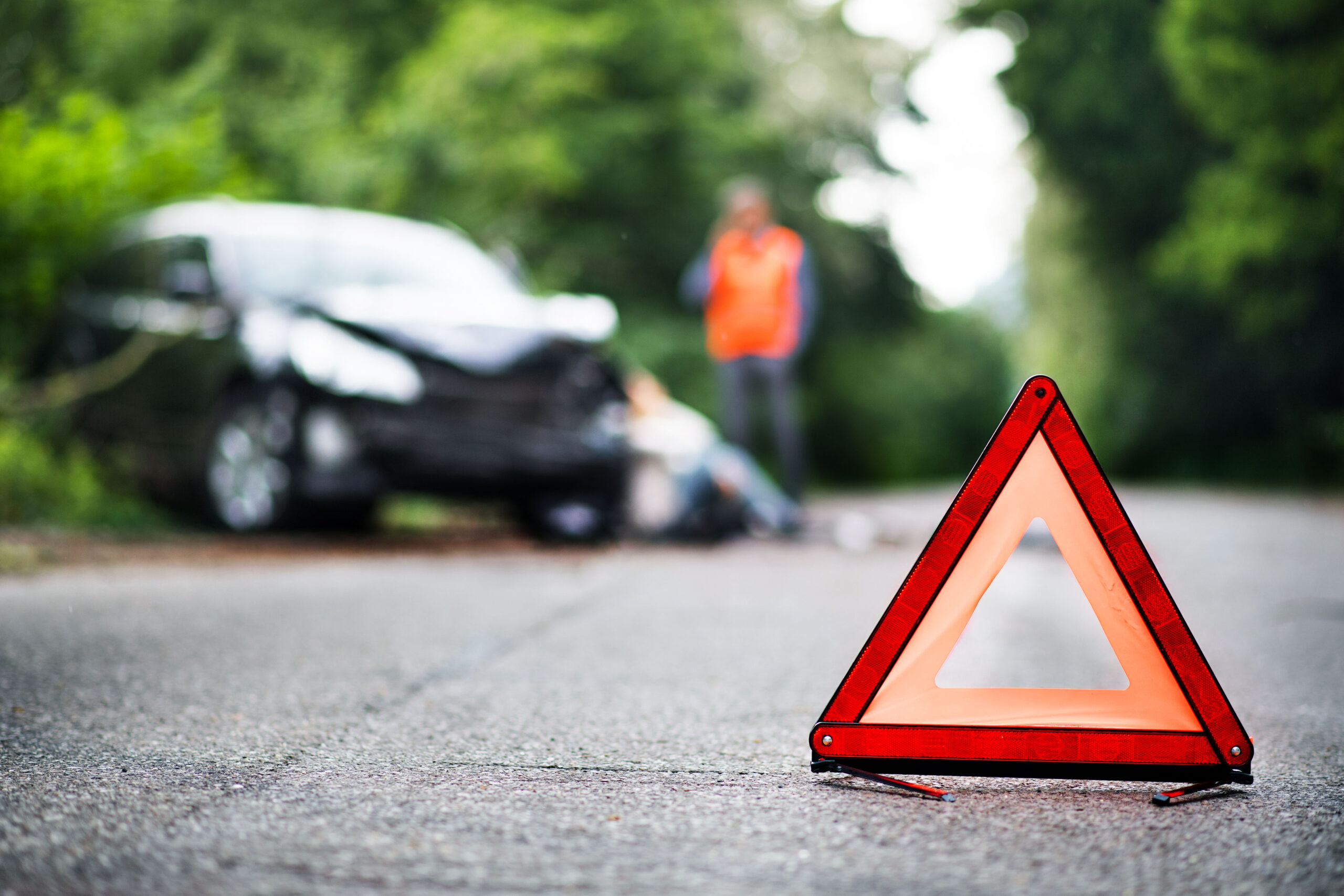 A close up of a red emergency triangle on the road in front of a car after an accident.