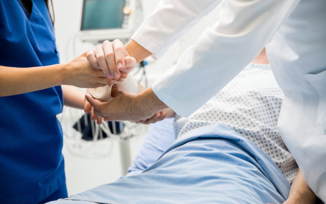 Closeup of the hands of two doctors bandaging a patient's arm in an emergency room