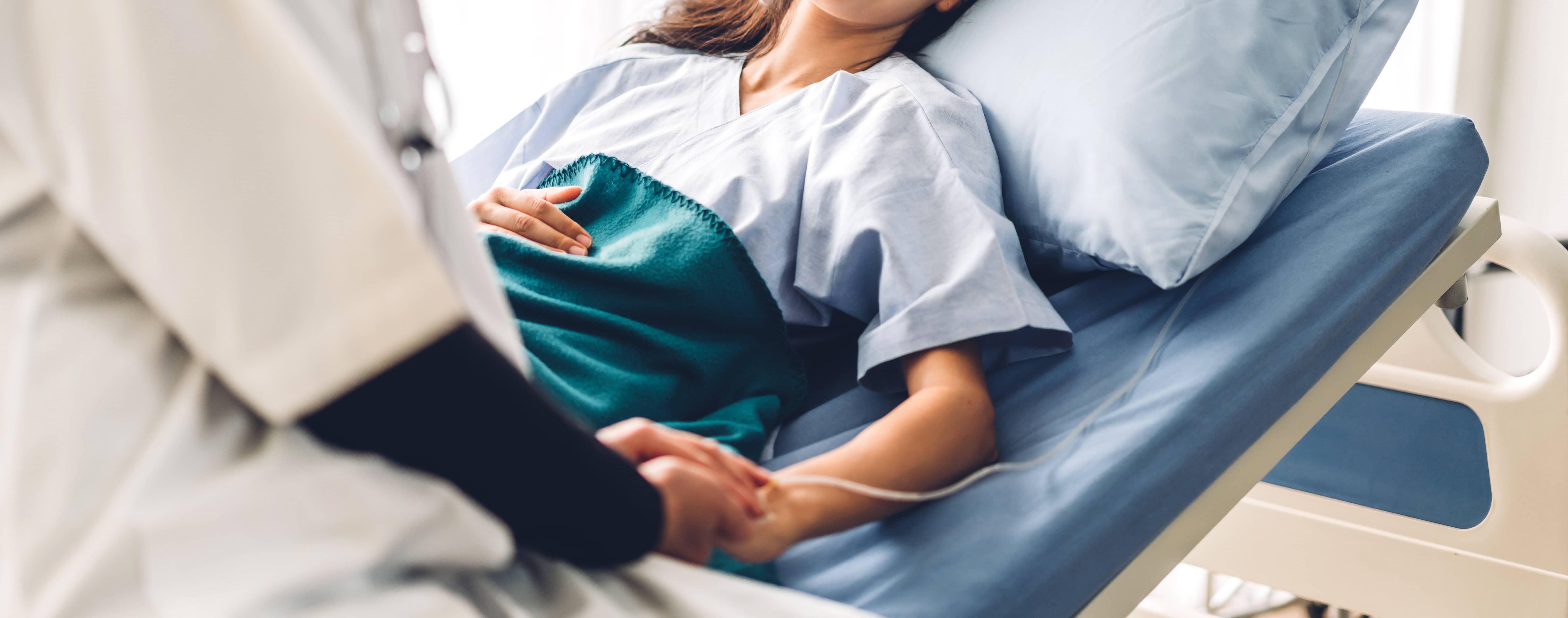 Female patient in hospital bed talking to doctor at bedside.