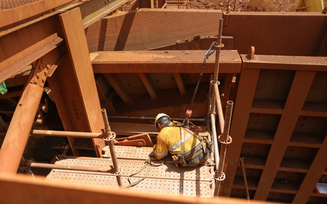 Scaffolder seating wearing safety helmet, fall arrest harness using clipping retractable device on the back of their safety harness loop attached to scaffold pole to preventing falling off working