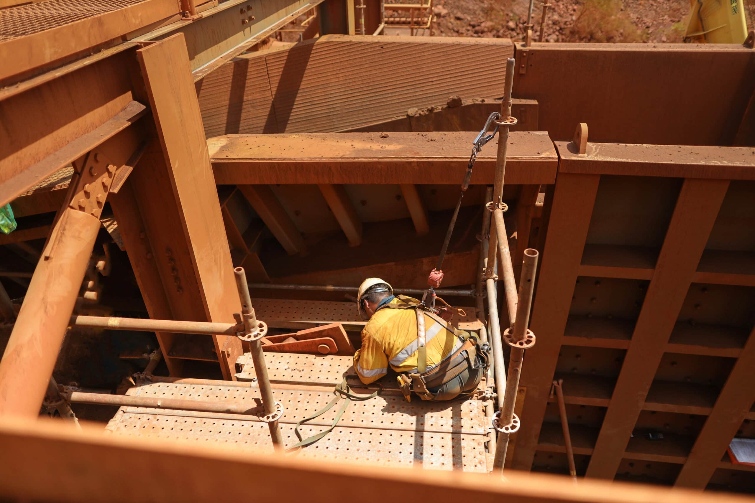 Scaffolder seating wearing safety helmet, fall arrest harness using clipping retractable device on the back of their safety harness loop attached to scaffold pole to preventing falling off working