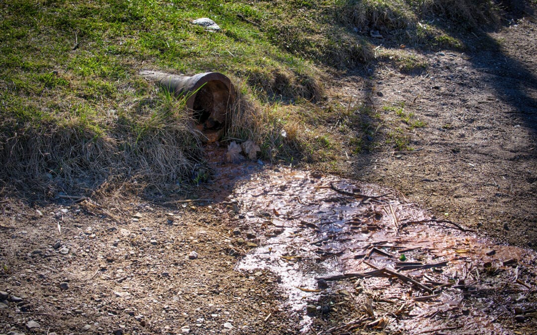Polluted Water Flowing From a Rusty Drain Pipe Into Contaminated Soil in a Rural Outdoor Environment