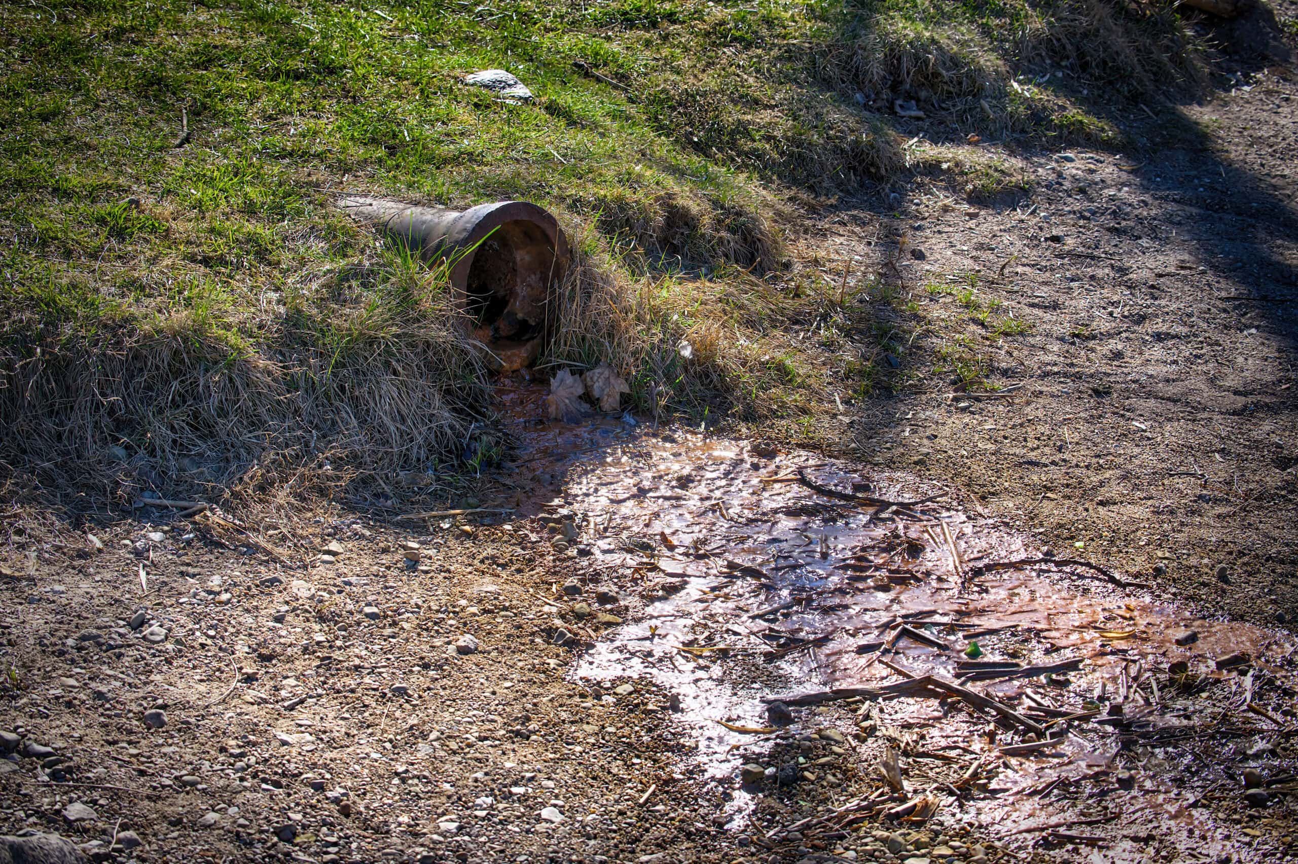 Polluted Water Flowing From a Rusty Drain Pipe Into Contaminated Soil in a Rural Outdoor Environment