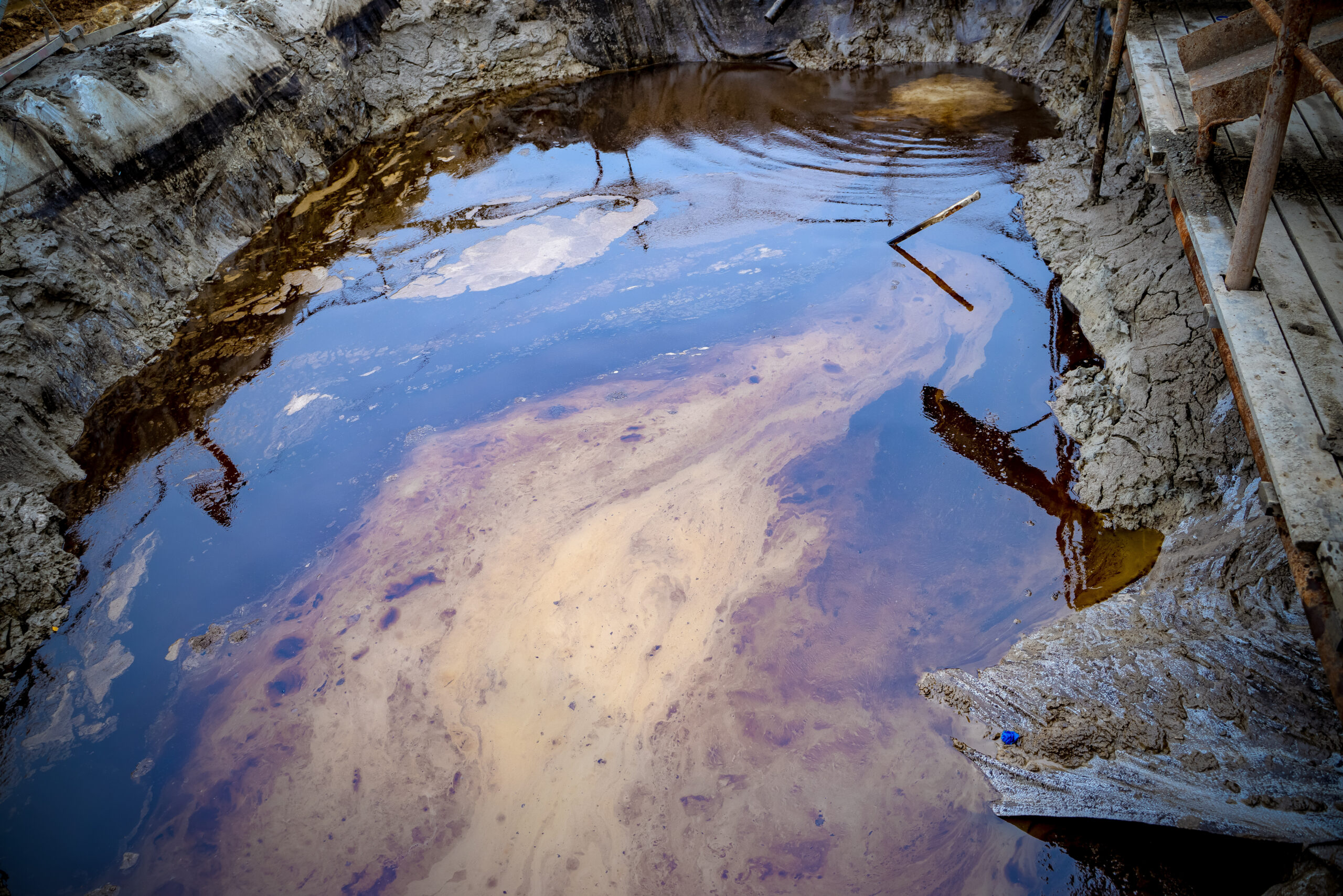 Oil and garbage pollution in the water. Selective focus with shallow depth of field. Iridescent colors abstract shapes on tar water surface of natural asphalt pit. Oil and garbage pollution in the water. Selective focus with shallow depth of field. Iridescent colors abstract shapes on tar water surface