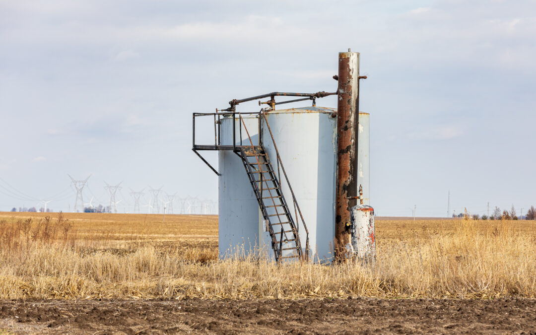 Old oil well storage tanks in farm field. Oil well abandonment, environment pollution, and oil production concept