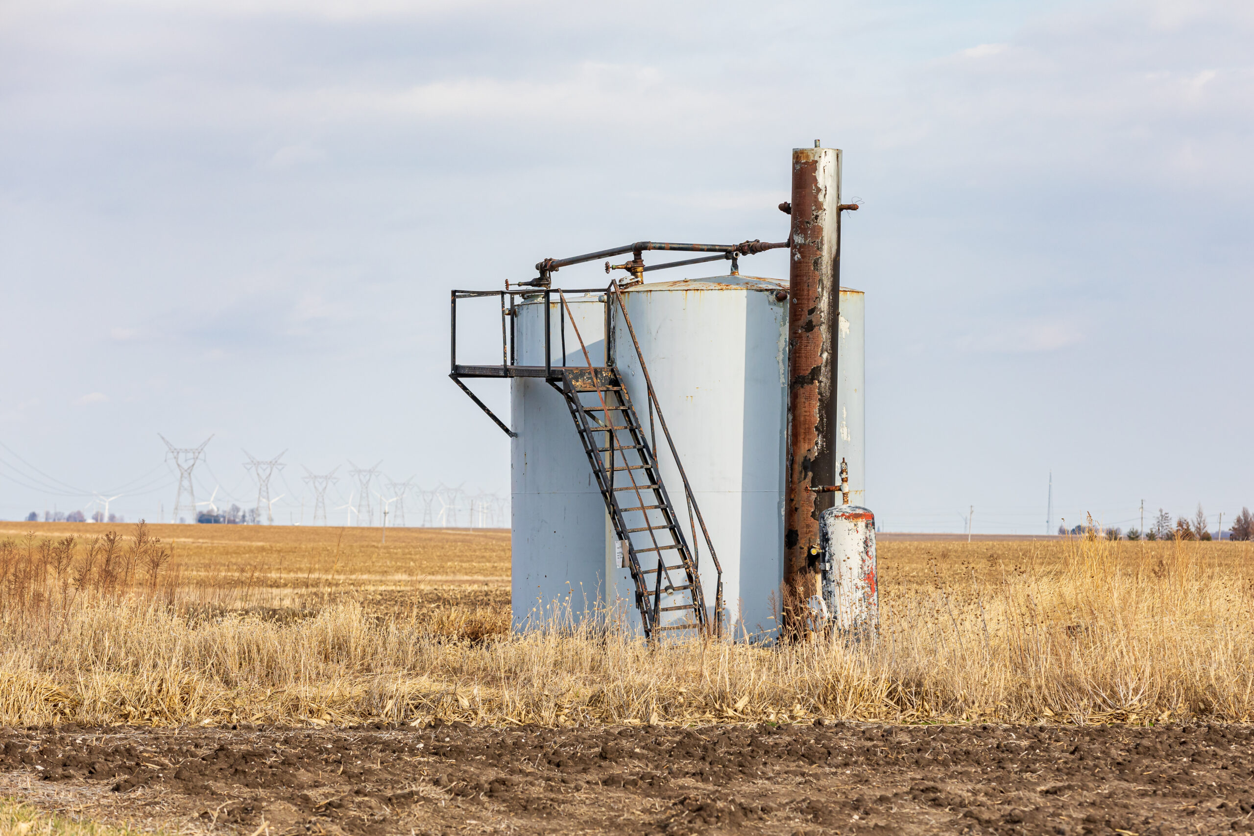 Old oil well storage tanks in farm field. Oil well abandonment, environment pollution, and oil production concept