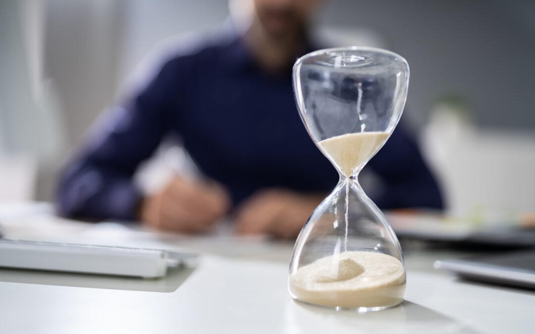 sand falling in an hourglass with person sitting at desk in background