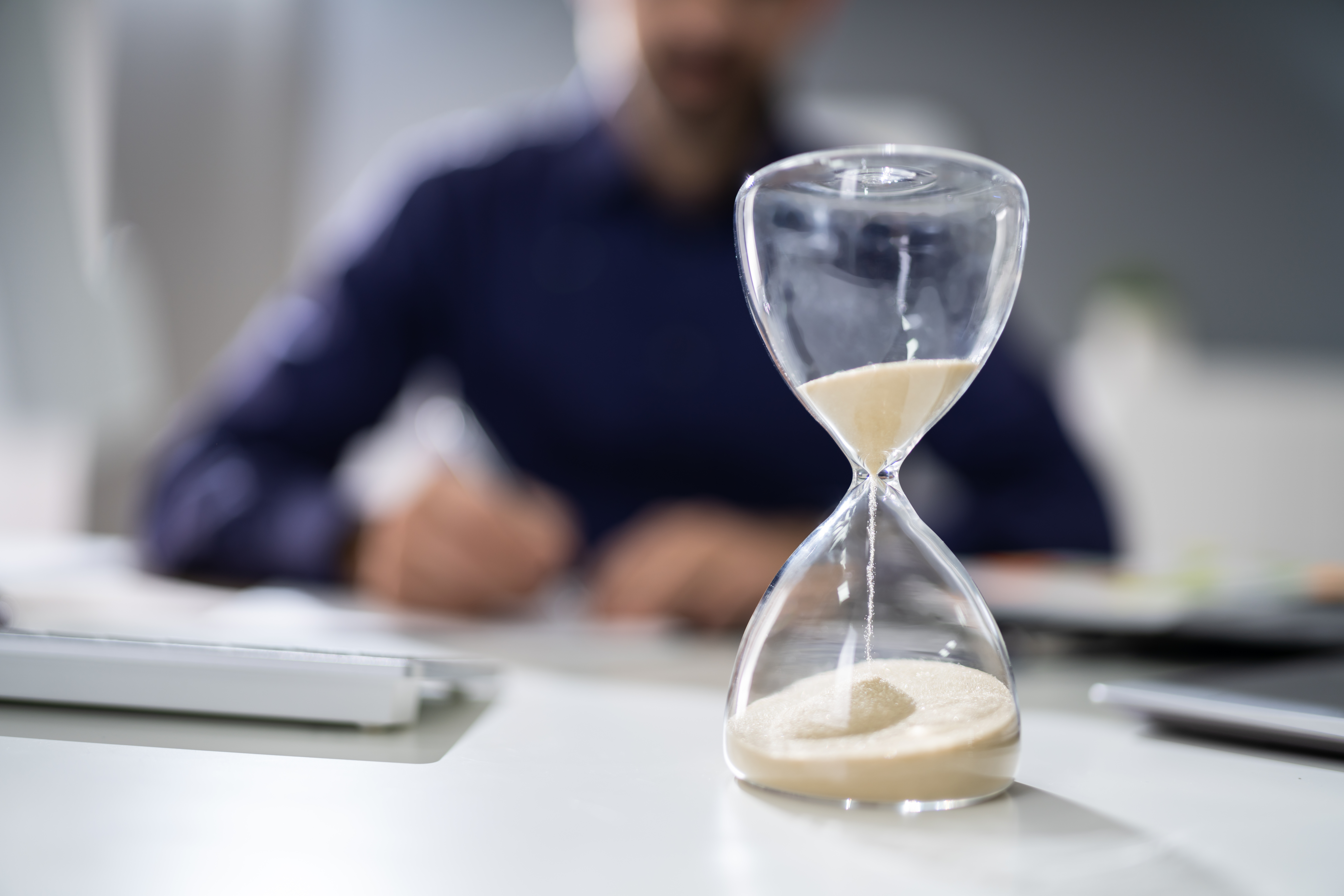sand falling in an hourglass with person sitting at desk in background